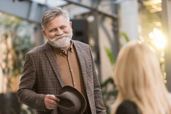 Selective focus of smiling senior man with hat looking at woman at table in restaurant — Stock Photo