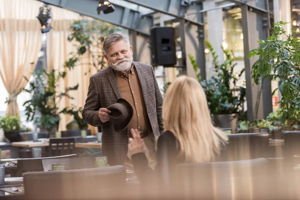 Selective focus of smiling senior man with hat looking at woman at table in restaurant — Stock Photo