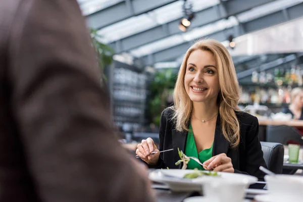 Частичный взгляд на мужчину и улыбающуюся женщину, обедающую вместе в ресторане — стоковое фото