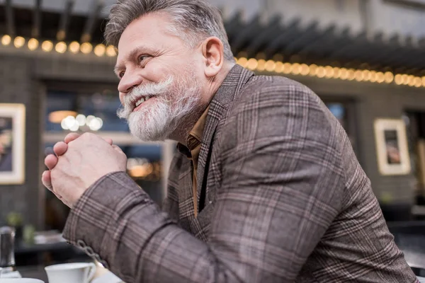 Side view of smiling senior man in stylish jacket in cafe — Stock Photo