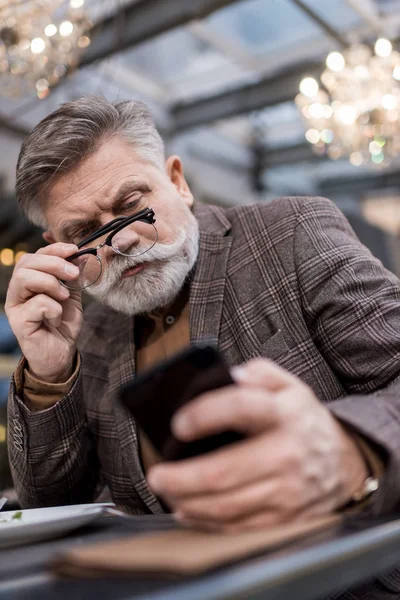 Messa a fuoco selettiva di uomo d'affari utilizzando smartphone in caffè — Foto stock