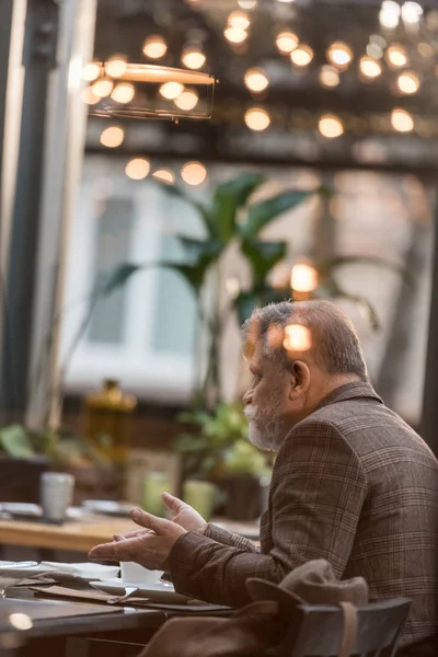 Side view of senior man sitting at table with cup of coffee during meeting in cafe — Stock Photo