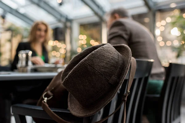 Selektiver Fokus von Hut auf Stuhl und Paar am Tisch im Café — Stockfoto