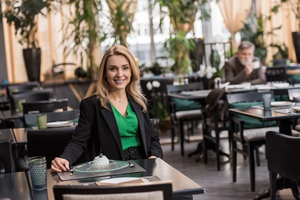 Портрет усміхненої жінки, що сидить за столом з десертом у кафе — стокове фото