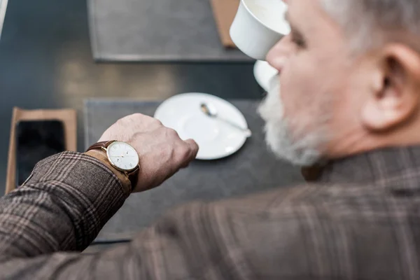 Селективное внимание старшего бизнесмена, проверяющего время, сидя за столом в кафе — стоковое фото