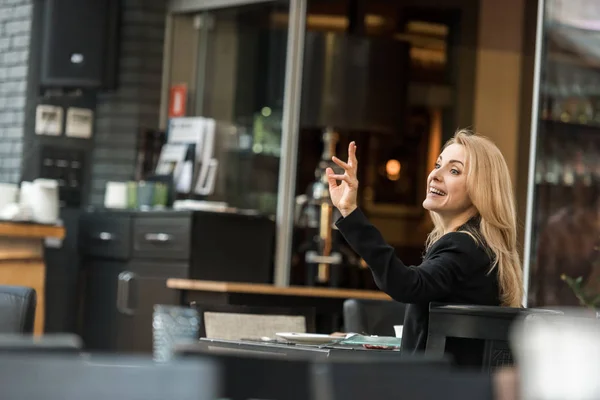 Вид збоку усміхненої жінки, яка кличе офіціанта в ресторані — стокове фото