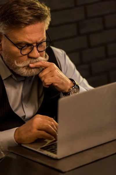 Side view of focused senior businessman working on laptop in cafe — Stock Photo