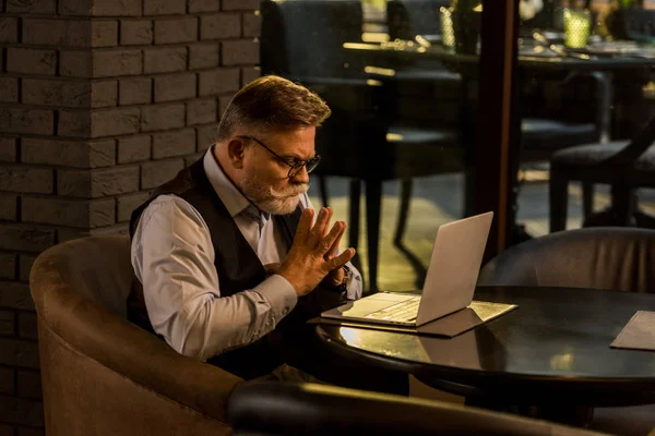 Vista lateral del hombre de negocios senior pensativo mirando la pantalla del ordenador portátil en la cafetería - foto de stock