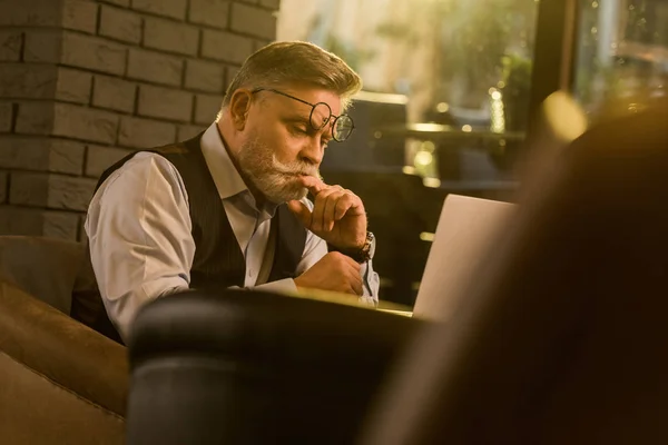 Side view of pensive senior businessman looking at laptop screen in cafe — Stock Photo