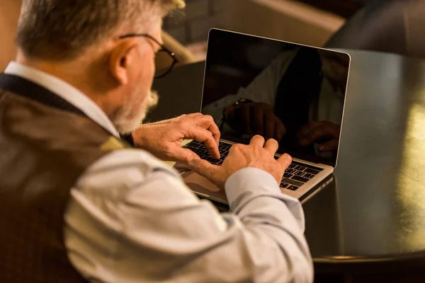 Selective focus of senior businessman typing on laptop in cafe — Stock Photo