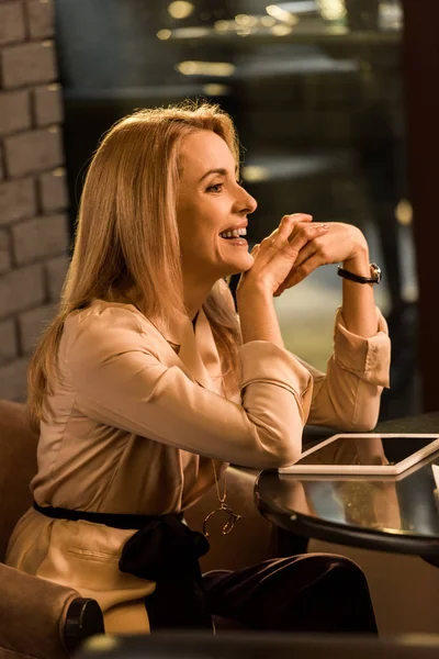 Vue latérale de la femme d'affaires souriante assise à table avec tablette — Photo de stock