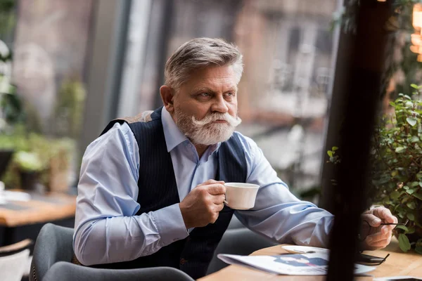 Retrato de hombre mayor barbudo con taza de café sentado una mesa en la cafetería - foto de stock