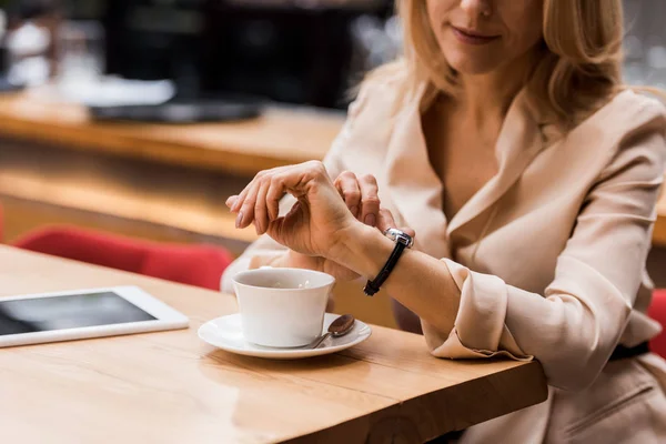 Recortado disparo de la mujer de negocios comprobar el tiempo mientras está sentado en la mesa con la tableta y la taza de café - foto de stock