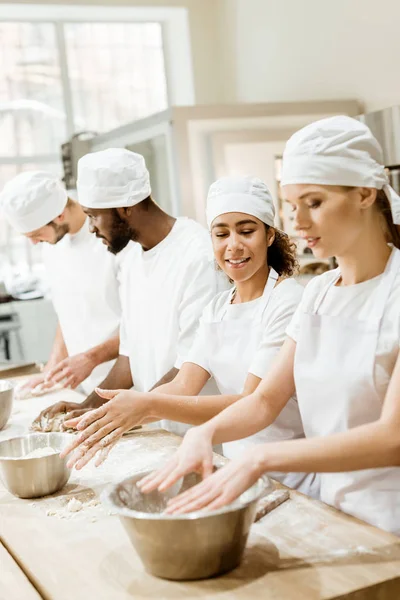 Group of young multiethnic baking manufacture workers kneading dough together — Stock Photo