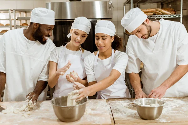 Group of young baking manufacture workers kneading dough together — Stock Photo