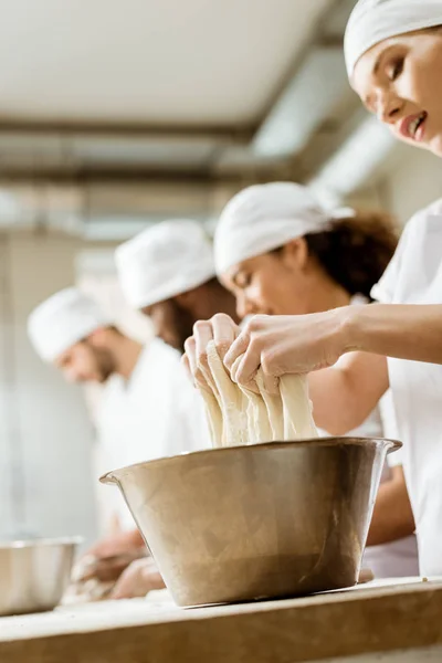 Close-up shot of group of baking manufacture workers kneading dough together — Stock Photo