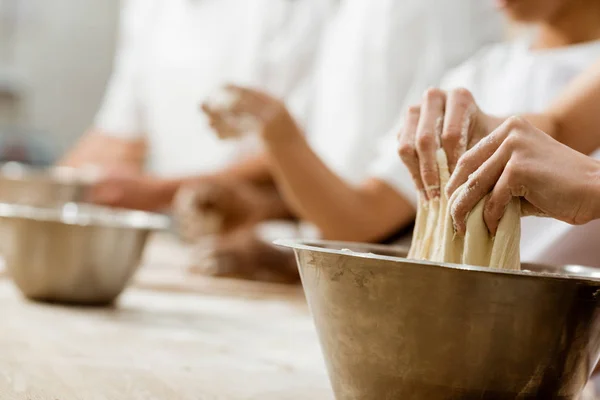 Cropped shot of baking manufacture workers kneading dough together — Stock Photo