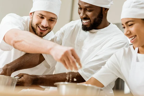 Laughing group of baking manufacture workers kneading dough together — Stock Photo