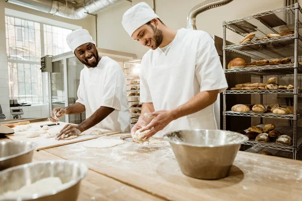 Happy bakers kneading dough together at baking manufacture and talking — Stock Photo