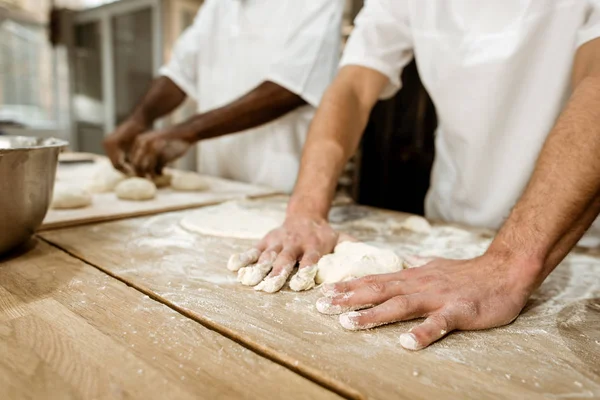 Cropped shot of bakers kneading dough together at baking manufacture — Stock Photo