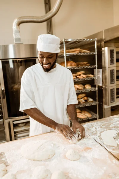 Sorridente panettiere africano americano preparare pasta cruda per pasticceria sulla fabbricazione di cottura al forno — Foto stock