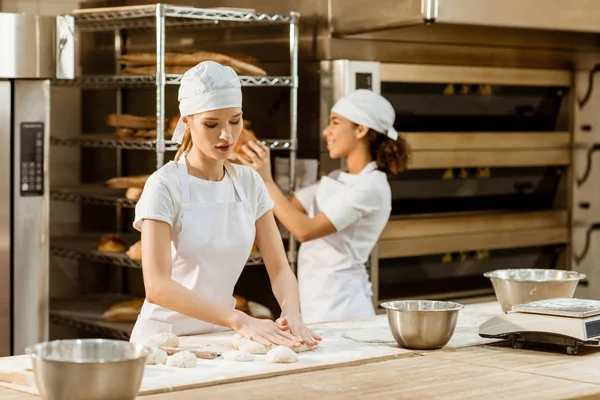 Panaderos femeninos atractivos jóvenes que trabajan juntos en la fabricación de hornear - foto de stock