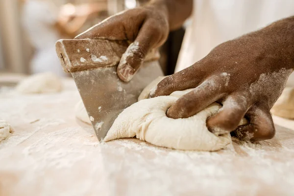 Cropped shot of baker cutting raw dough with dough knife — Stock Photo