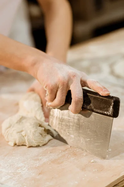 Cropped shot of baker cutting dough with dough knife — Stock Photo