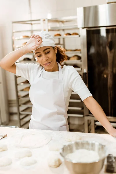 Overworked female baker wiping sweat from forehead at baking manufacture — Stock Photo