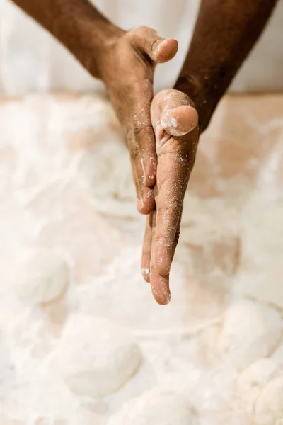Обрезанный кадр африканского американского пекаря, готовящего тесто для выпечки и закрывающего руки мукой — стоковое фото
