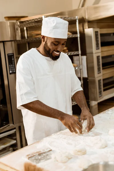 Sorridente panettiere africano americano preparare pasta sulla fabbricazione di cottura — Foto stock