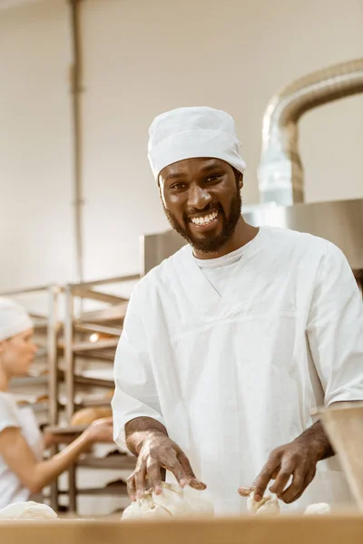 Handsome african american baker kneading dough on baking manufacture — Stock Photo