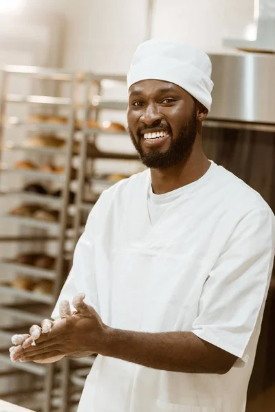 Apuesto panadero afroamericano con harina en las manos en la fabricación de la hornada - foto de stock