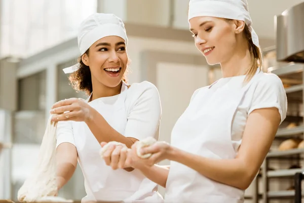 Happy female bakers kneading dough together at baking manufacture — Stock Photo