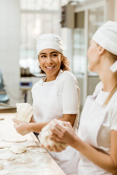 Happy female bakers kneading dough together at baking manufacture — Stock Photo
