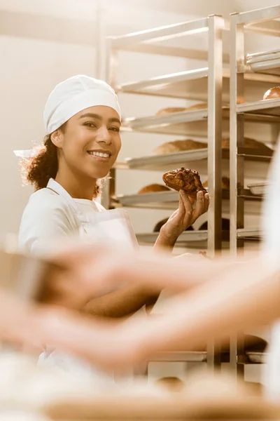 Beautiful female baker with delicious croissant on baking manufacture — Stock Photo