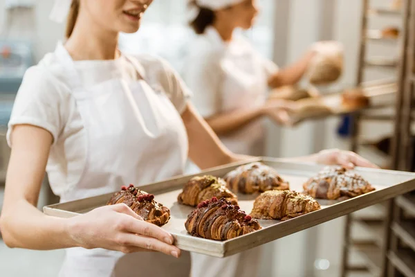 Cropped shot of young baker holding tray with fresh croissants at baking manufacture — Stock Photo