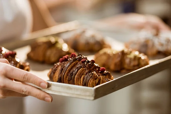 Abgeschnittene Aufnahme einer Bäckerin, die Blech mit leckeren Croissants auf Backherstellung hält — Stockfoto
