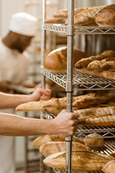 Cropped shot of baker holding shelves with fresh bread loaves at baking manufacture — Stock Photo
