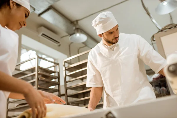 Jovens padeiros confiantes que trabalham com rolo de massa industrial na fabricação de cozimento — Fotografia de Stock