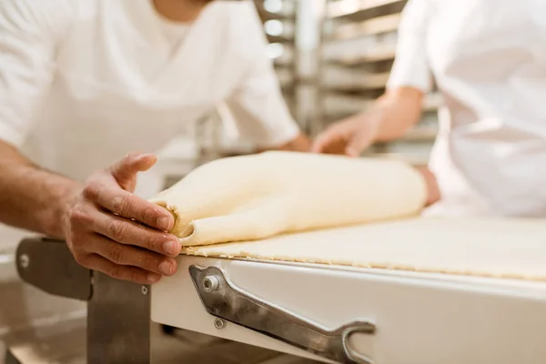 Cropped shot of bakers rolling dough with industrial dough roller at baking manufacture — Stock Photo