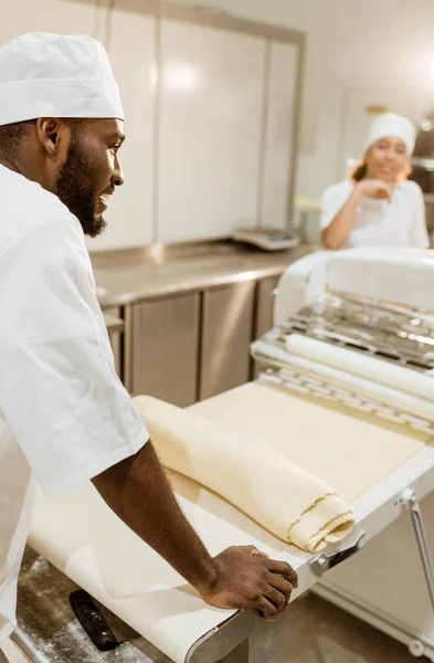 African american baker with roll of raw dough on baking manufacture — Stock Photo