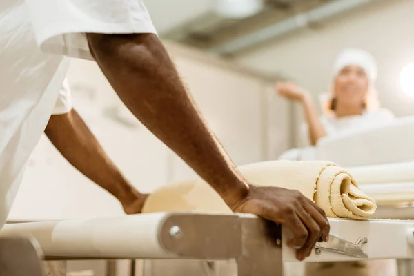 Обрезанный кадр пекарей, работающих с промышленным тестовым роликом при производстве выпечки — стоковое фото
