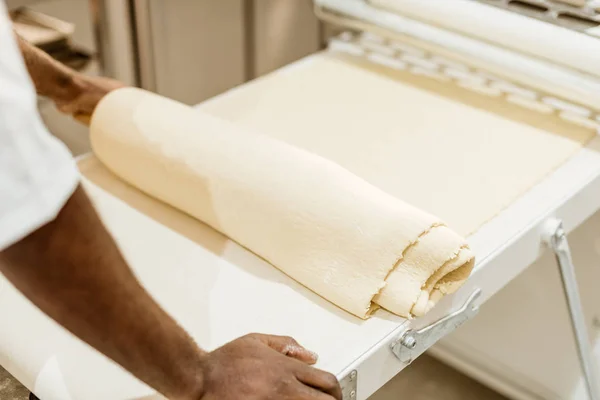 Cropped shot of african american baker with roll of raw dough on baking manufacture — Stock Photo