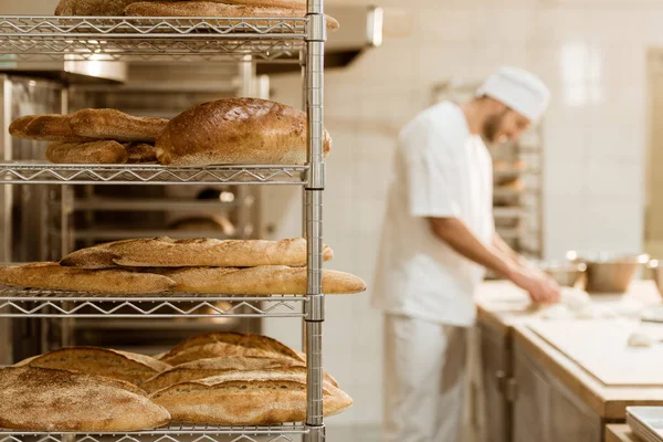 Shelves with fresh bread and blurred baker on background at baking manufacture — Stock Photo