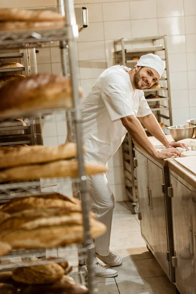 Panadero joven sonriente con masa cruda en el lugar de trabajo en la fabricación de la hornada - foto de stock
