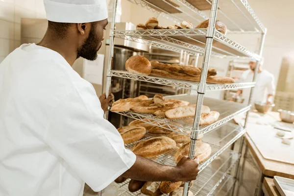 Baker driving shelves of fresh bread on baking manufacture — Stock Photo