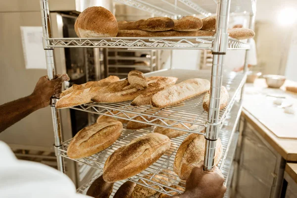 Abgeschnittener Schuss von Bäcker fährt Regale mit frischem Brot auf Backherstellung — Stockfoto