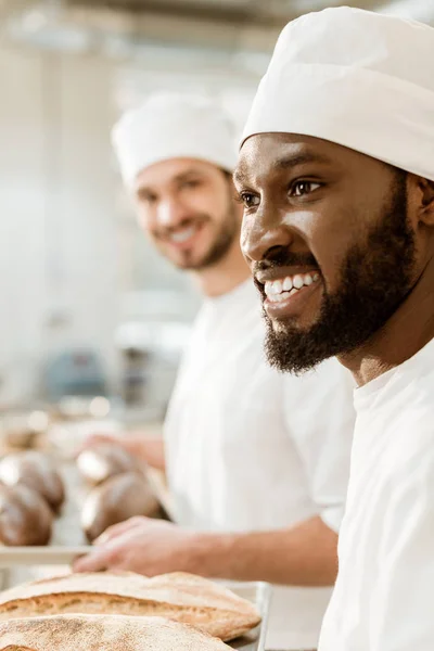 Handsome young bakers in hats at baking manufacture — Stock Photo