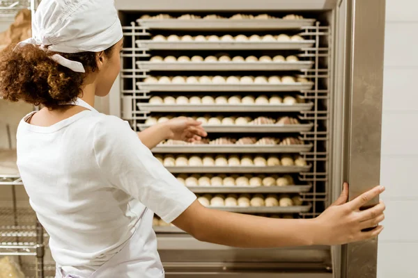 Female baker pointing at dough inside of industrial oven at baking manufacture — Stock Photo